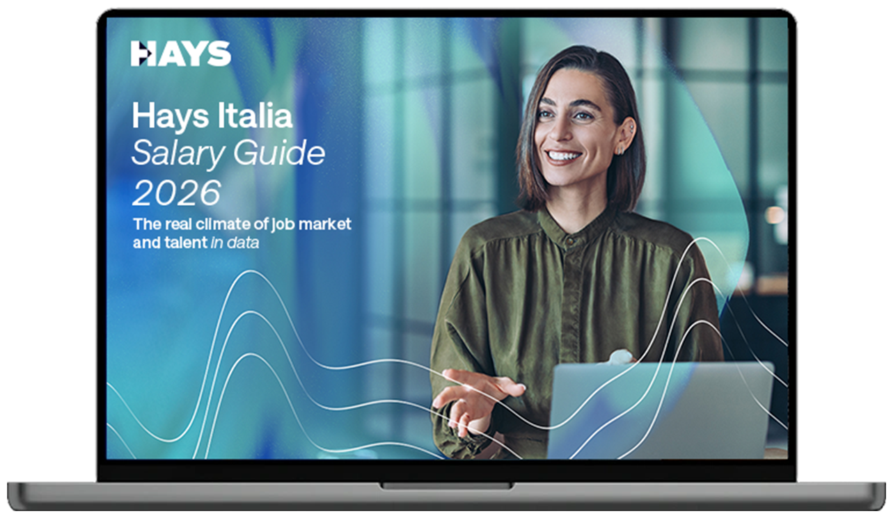 Computer portatile che mostra la copertina della Guida salariale 2026 di Hays Italia, con un professionista che fa una presentazione in un moderno ufficio