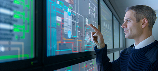Professionista che interagisce con un grande display digitale che mostra dati tecnici complessi e diagrammi di sistema